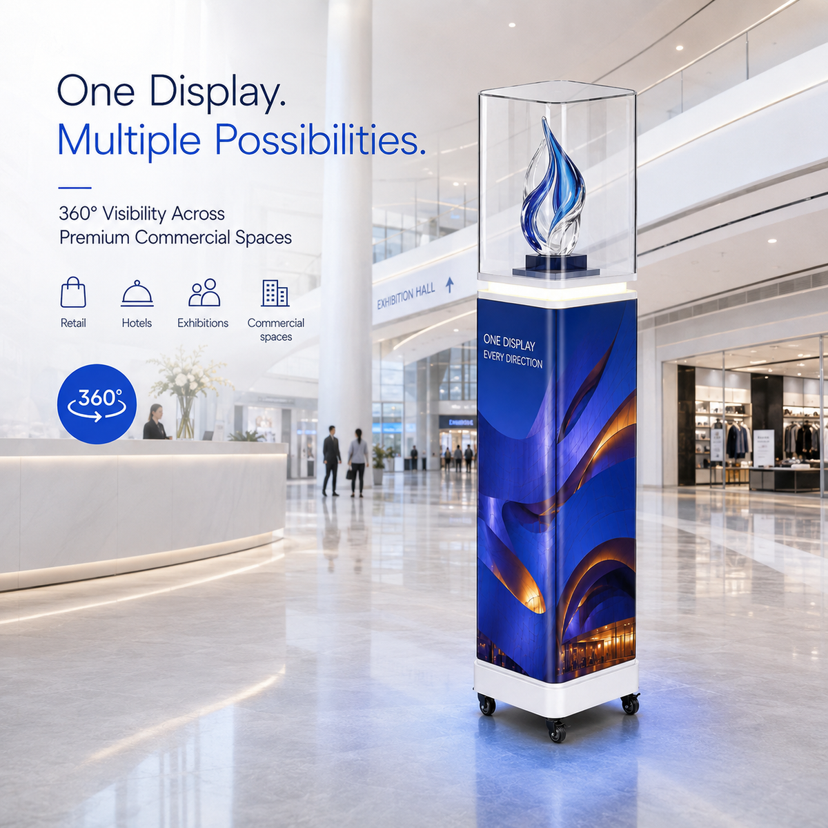 A freestanding illuminated display pedestal in a modern shopping mall interior. The unit has a clear top section with a blue flame-like light and a blue-and-purple printed wrap around the sides, mounted on a white base with caster wheels.